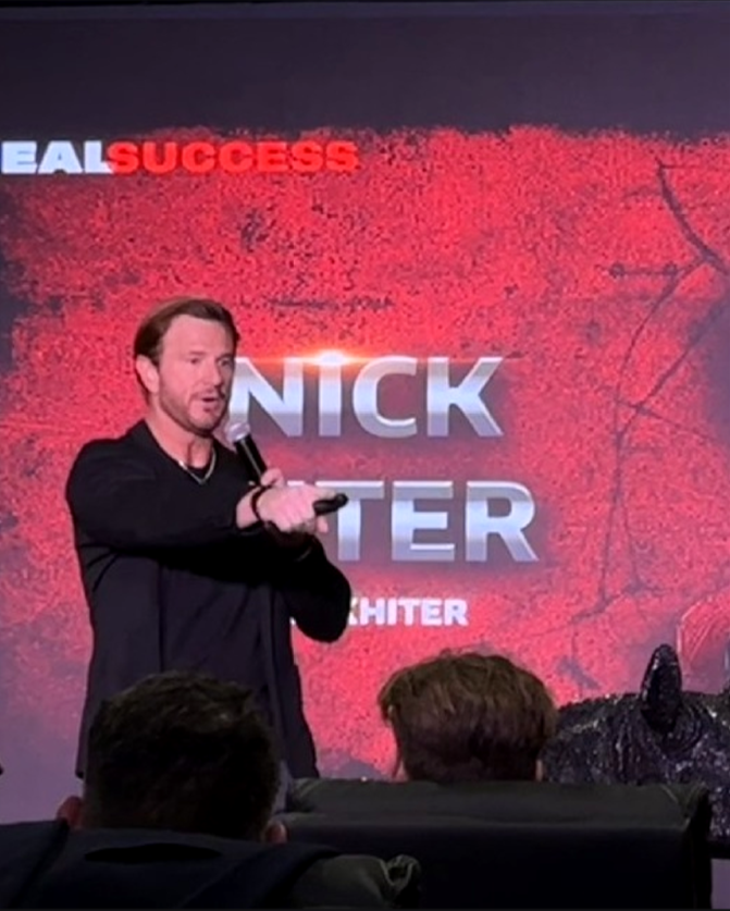 Nick Hiter speaking on stage with a microphone at a REALSUCCESS personal branding workshop
